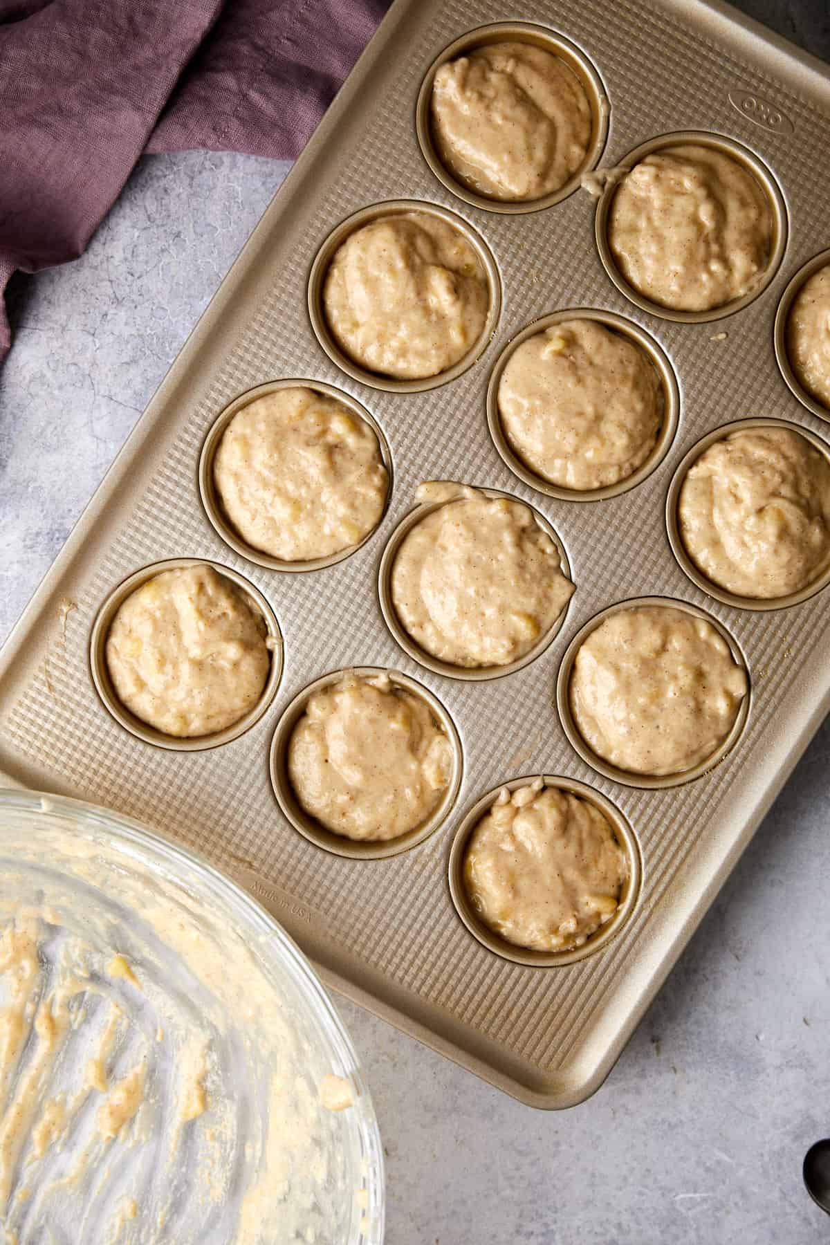 overhead view of muffin tin with cinnamon banana muffin batter filled in all of the tin cups. 