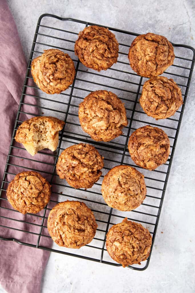 Overhead view of cinnamon banana muffins on a wire rack with a bite bitten out of one muffin. 