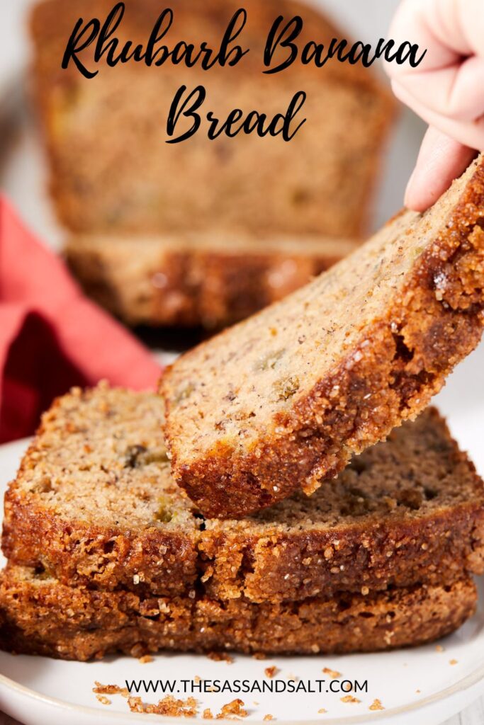 A hand lifts a slice of moist banana rhubarb bread from a stack on a plate. The loaf’s golden, crispy crust and bits of rhubarb stand out. Text reads “Rhubarb Banana Bread” with a link to the banana rhubarb bread recipe below.