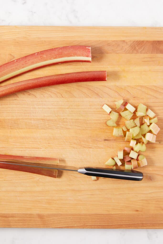 overhead view of a rhubarb stalk being cut with a knife down the center of the stalk.