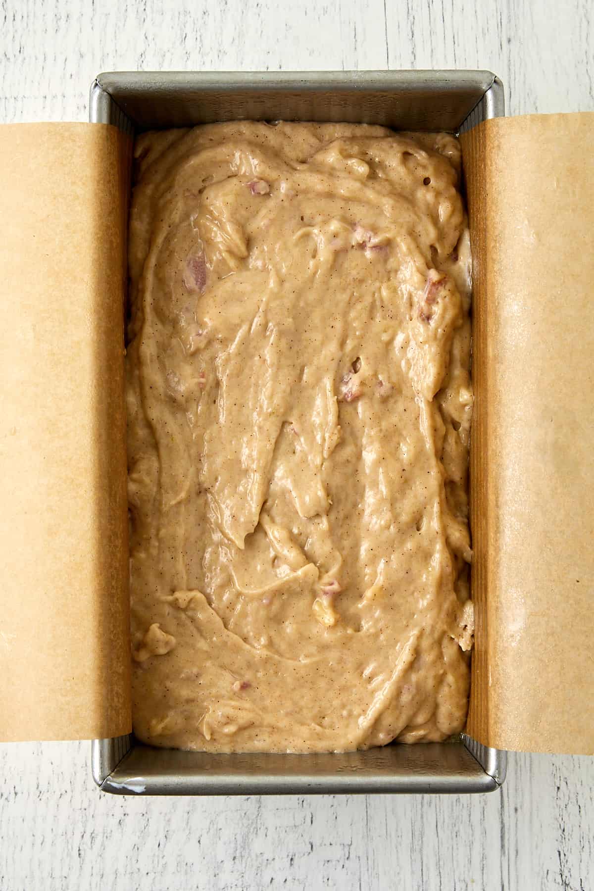 overhead view of rhubarb banana bread batter in loaf pan lined with parchment paper.