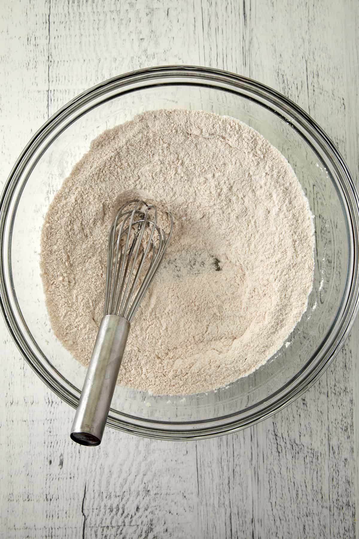 Overhead view of dry ingredients mixed together with a whisk in a glass mixing bowl.