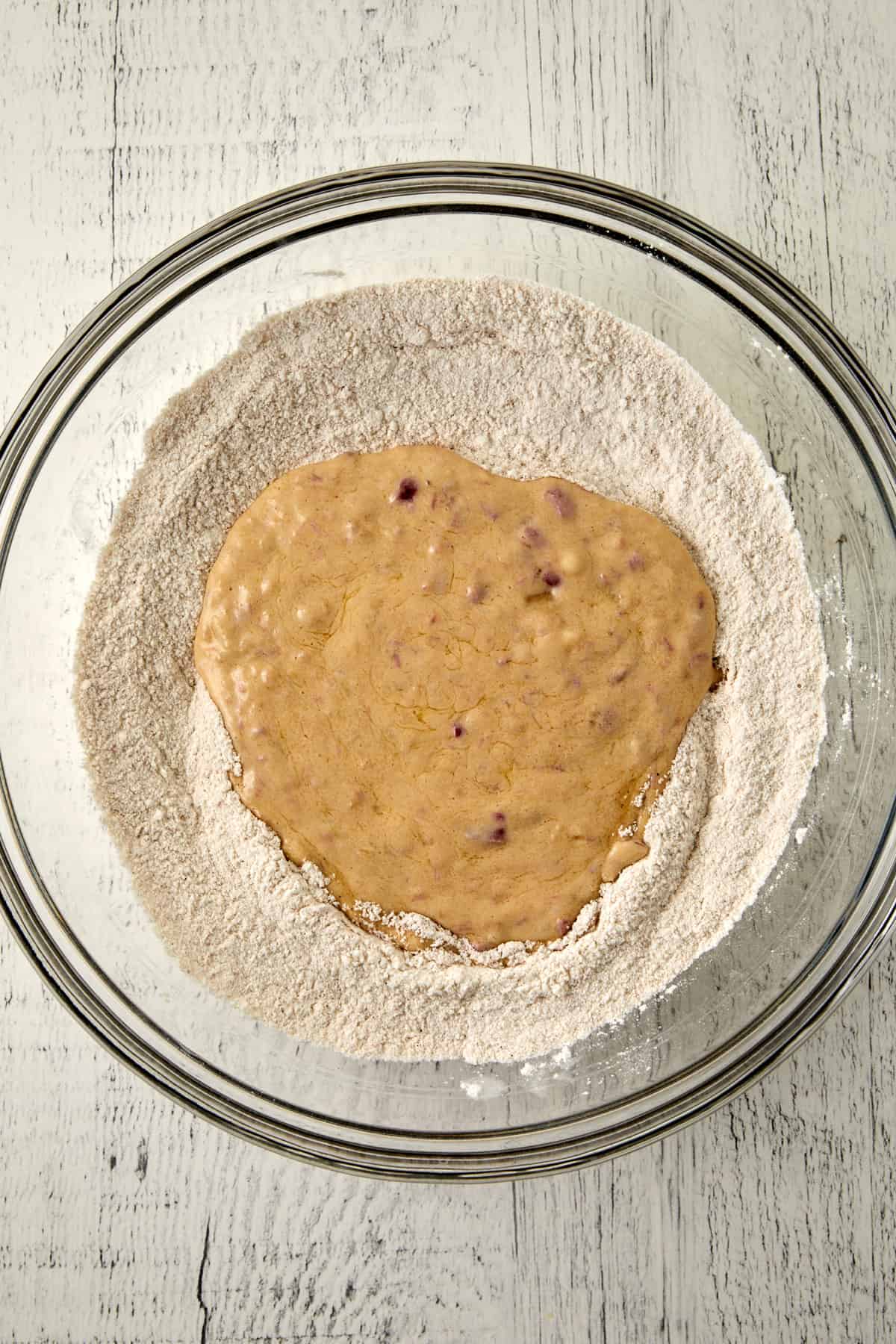 Overhead view of wet ingredients in dry ingredients in a glass mixing bowl.