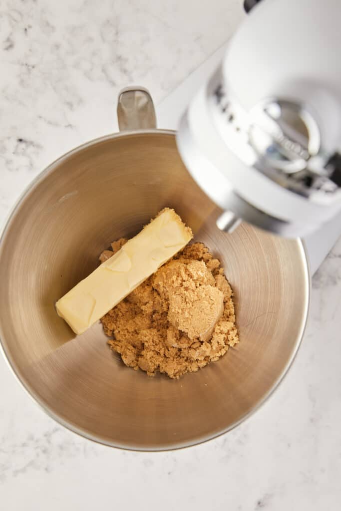 overheard view of a stick of butter and brown sugar in a mixing bowl.