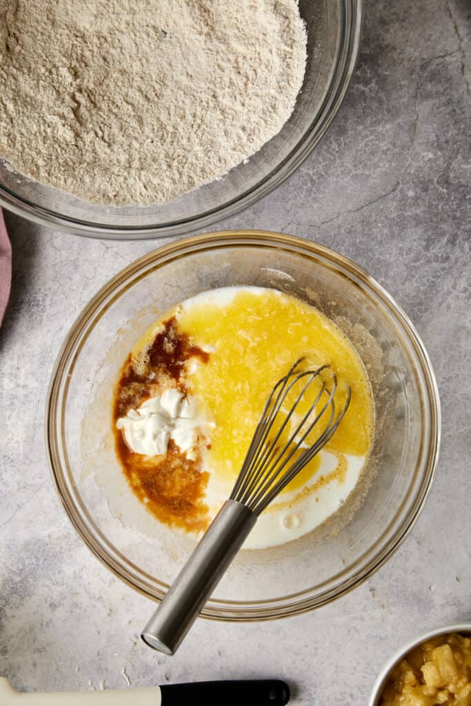 Overhead view of wet ingredients piled in a glass bowl with a whisk in the bowl.