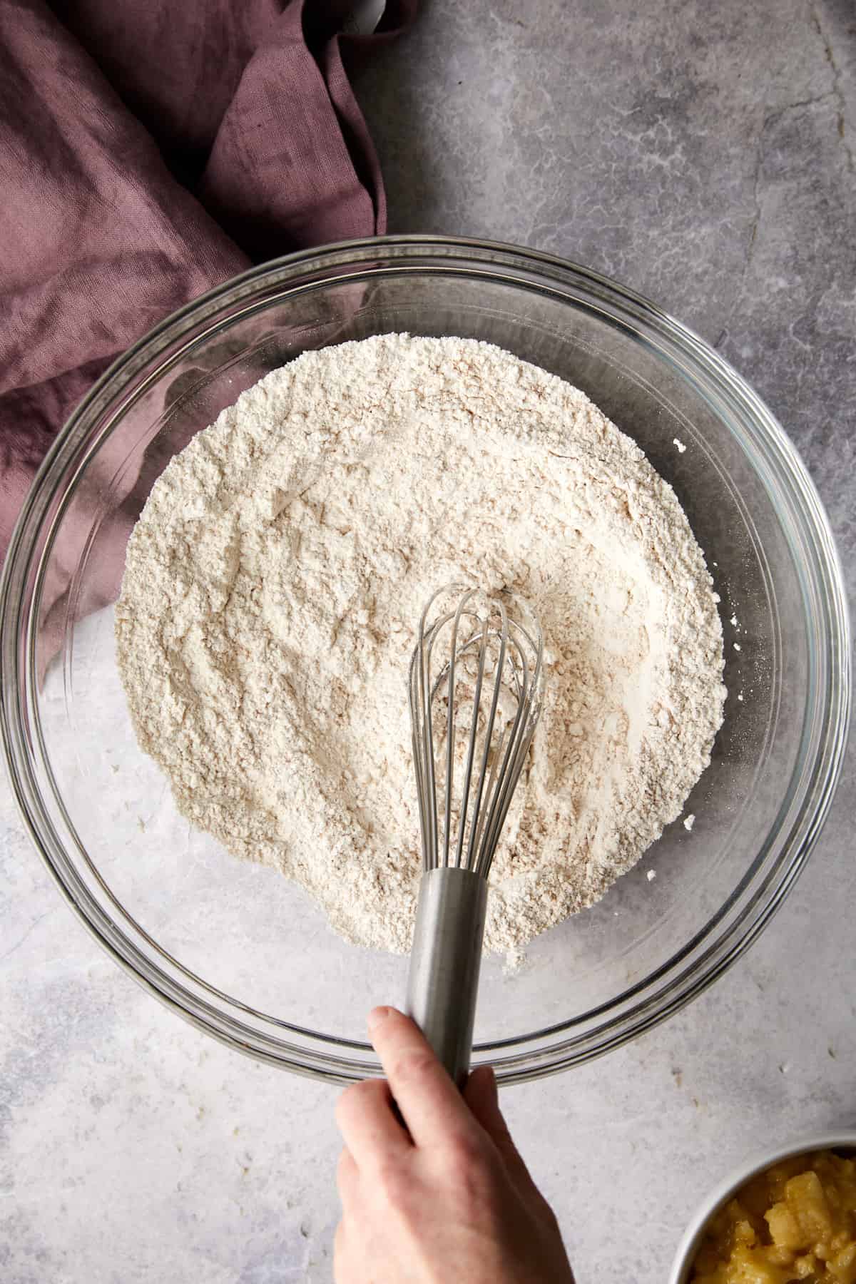Overhead view of dry ingredients mixed together with a hand on a metal whisk.
