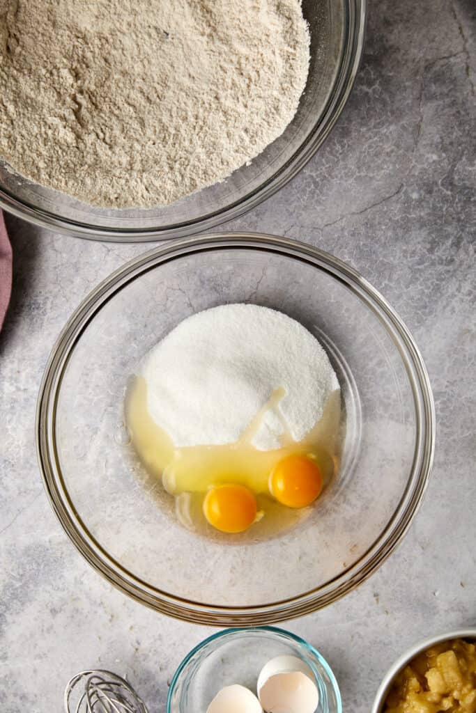 Overhead view of sugar and eggs in a glass bowl.