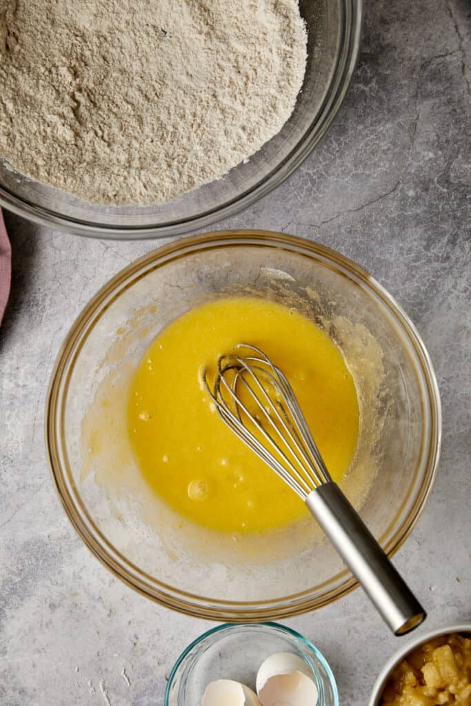 Overhead view of eggs and sugar mixed together in a glass mixing bowl.