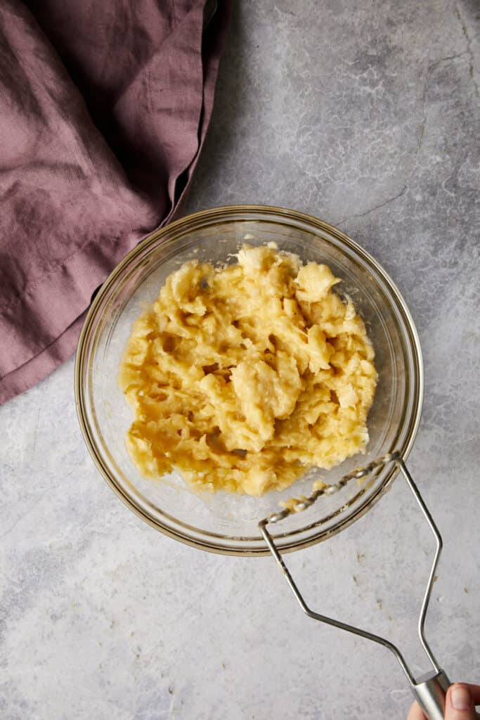 Overhead view of mashed bananas in a glass bowl.