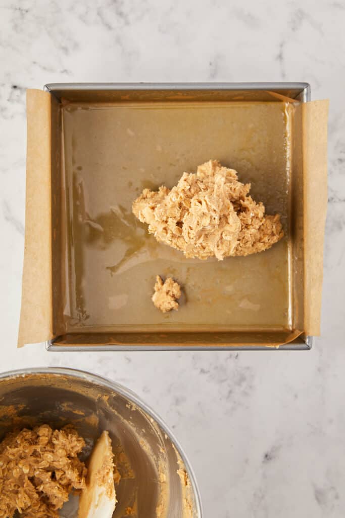 overhead view of a scoop of the dough in the 8x8 pan with the mixing bowl in the lower left corner with a spatula in the bowl.