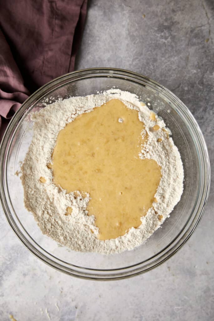 Overhead view of wet ingredients poured into the dry ingredients in a glass bowl.