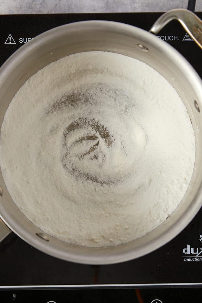 Overhead view of sugar and cornstarch in a stainless steel pot whisked together.