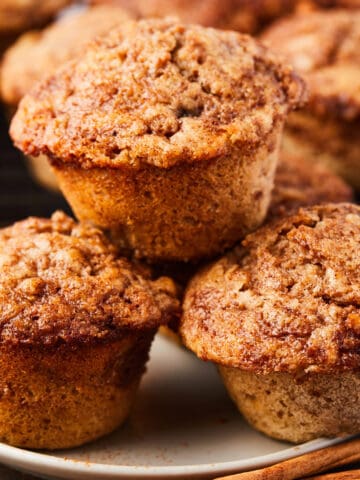 close up view of 3 baked cinnamon banana muffins on a white plate.