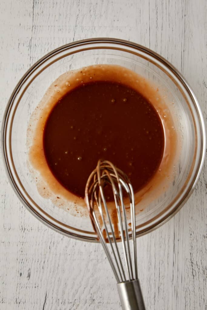 Overhead view of Nutella syrup mixed together in a glass bowl with a whisk.