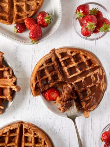 Overhead view of cooked Nutella waffles on white plates.