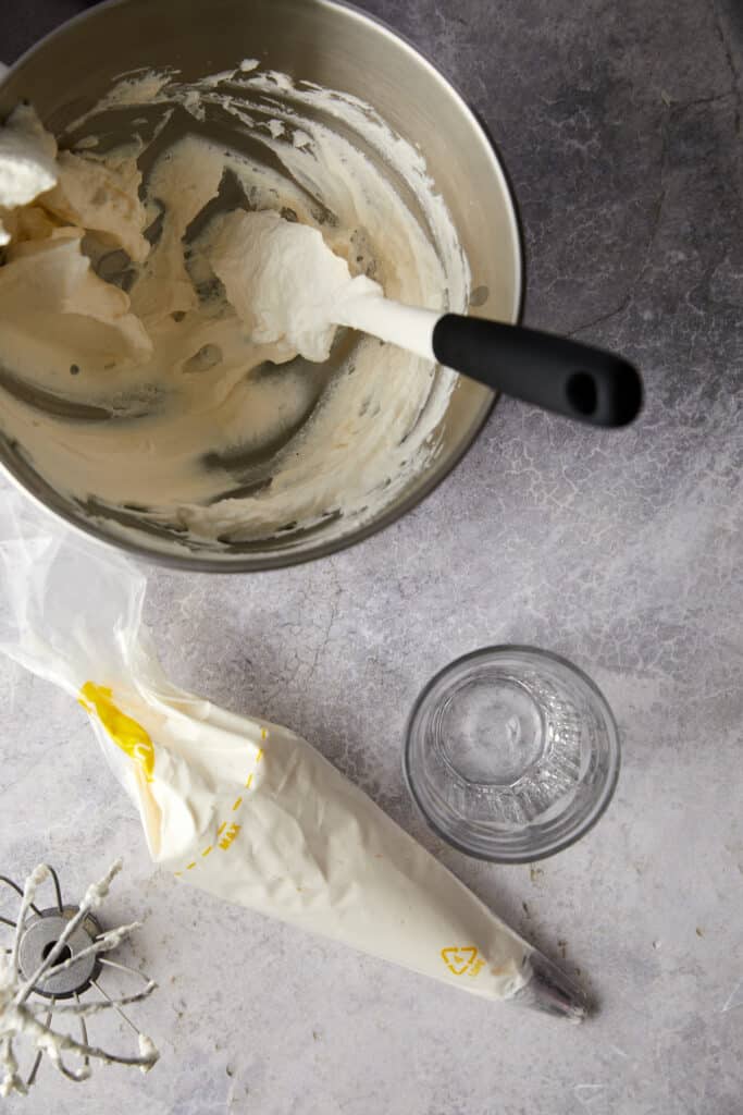 Overhead view of whipping cream stand mixer bowl with a spatula, a piping bag filled with the whipped cream. 