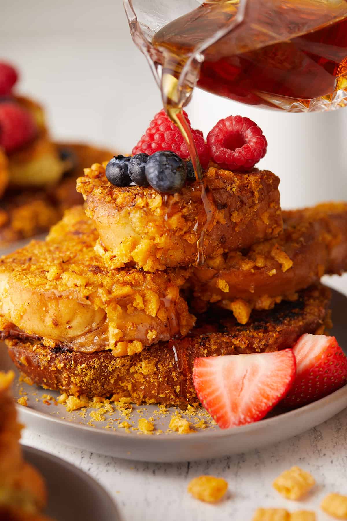 Close-up view of Captain Crunch French toast stacked on top of a plate with maple syrup being poured on top.