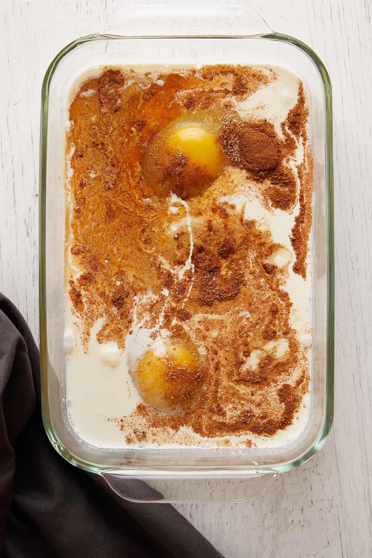 Overhead view of eggs, cinnamon, and cream in a glass pan