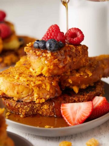 Close-up view of Captain Crunch French toast stacked on top of a plate with maple syrup being poured on top.