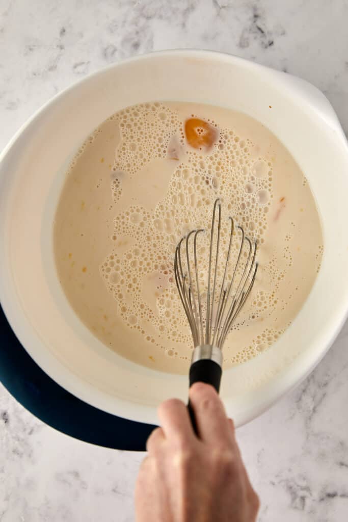 Overhead view of eggs, millk and vanilla being mixed with a whisk. 