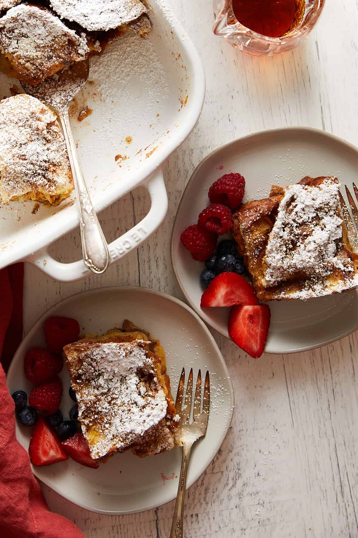 A plated serving of Challah French Toast Casserole topped with syrup and fresh berries.