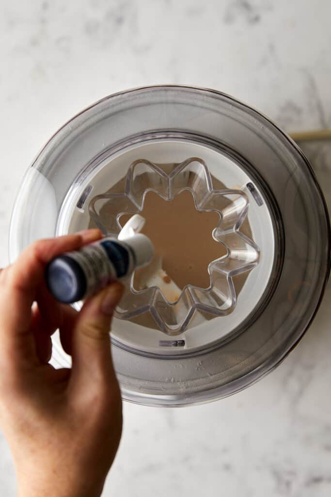 Fruity pebble ice cream mixture with drops of pink food coloring being poured into ice cream maker.