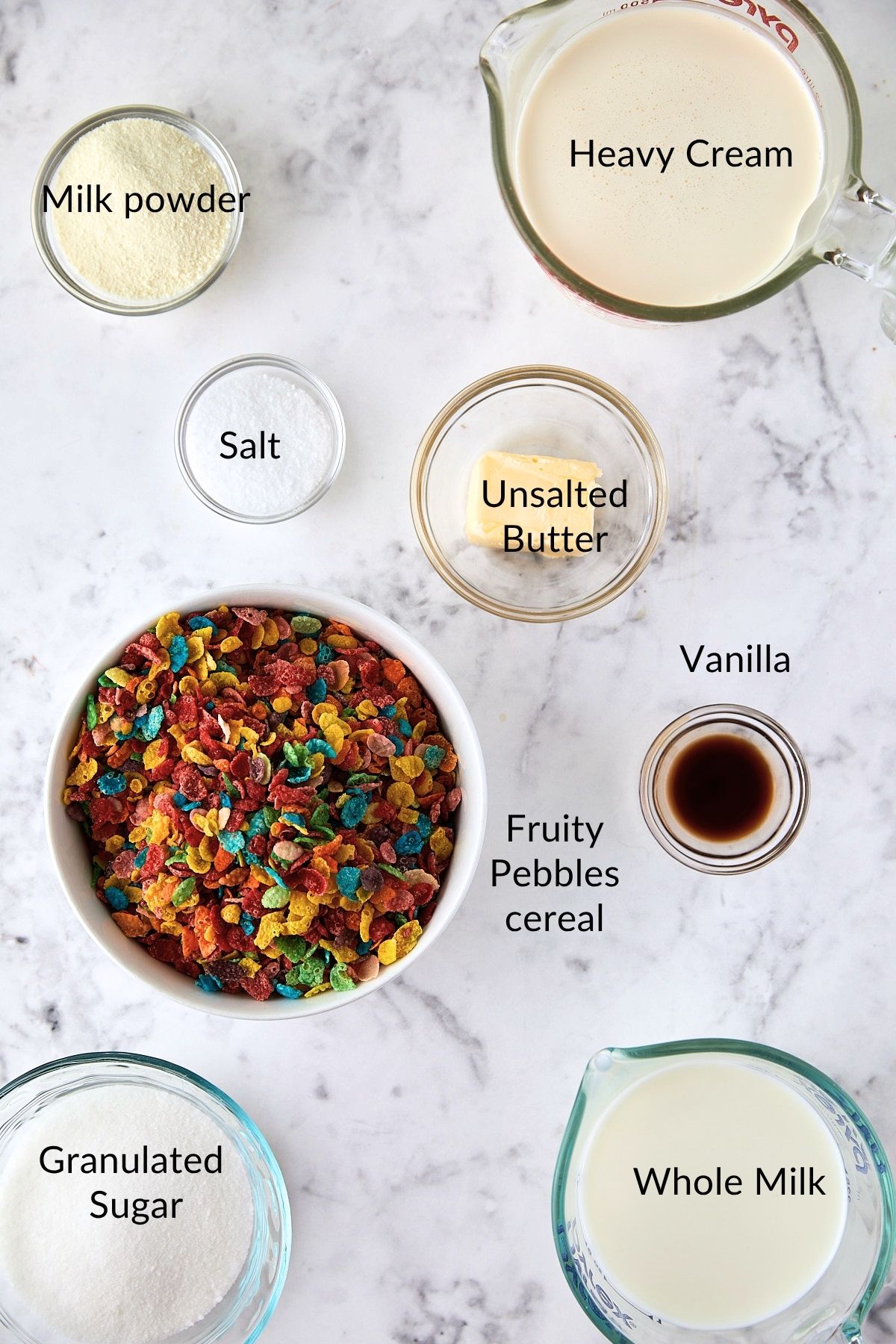 Ingredients for homemade Fruity Pebbles ice cream laid out on a marble surface.