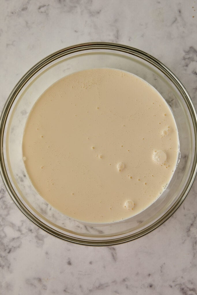 Overhead view of heavy cram and whole milk in a glass bowl sitting on a marbled surface. 