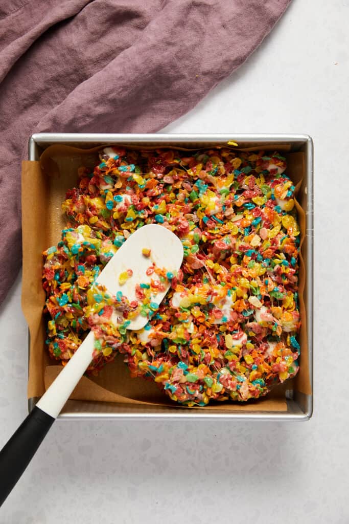 Overhead view of fruity pebbles marshmallow treats being spread into pan.