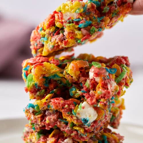 Fruity pebbles marshmallow treat stacked on top of each other with a hand grabbing one from the top.