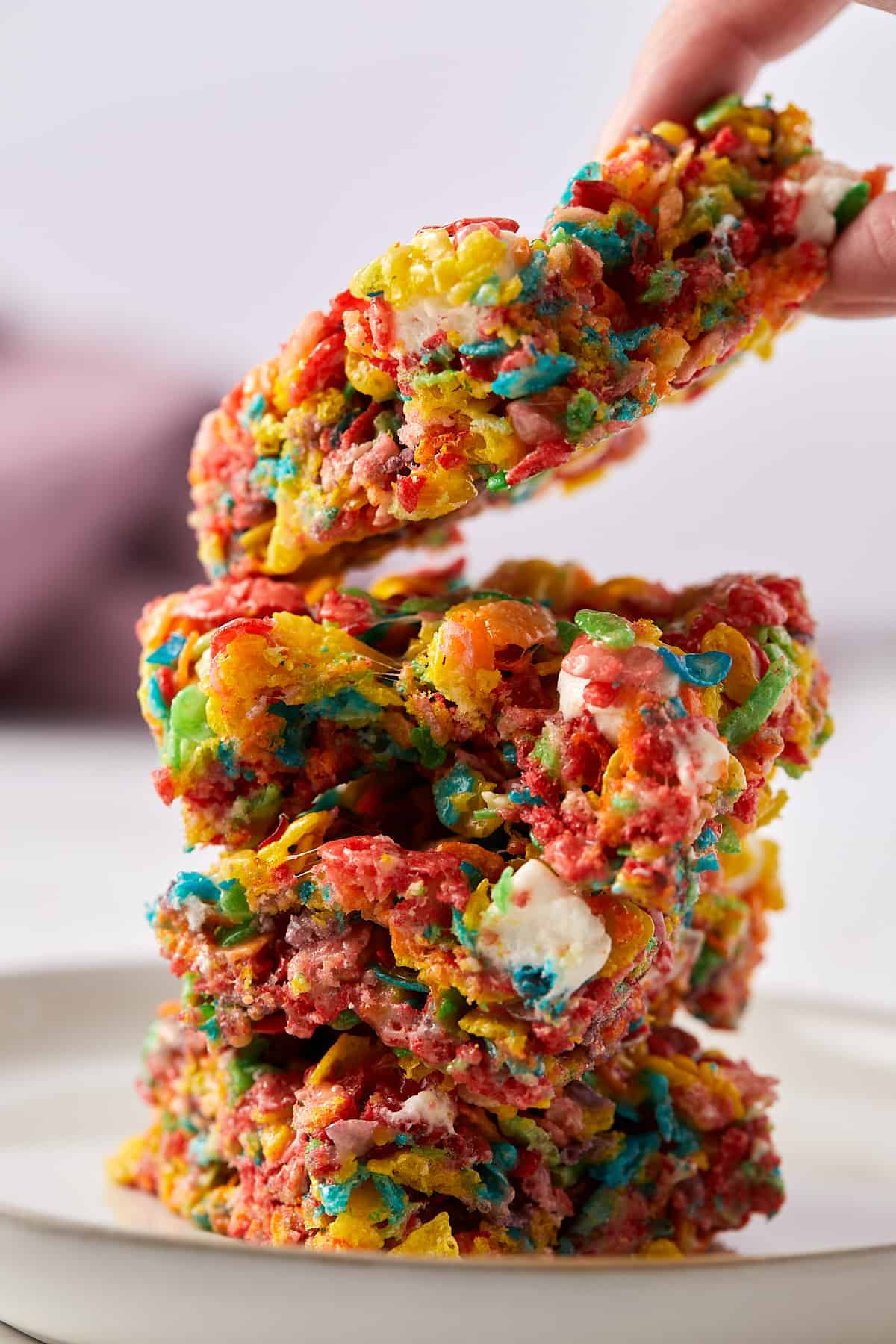 Fruity pebbles marshmallow treat stacked on top of each other with a hand grabbing one from the top.