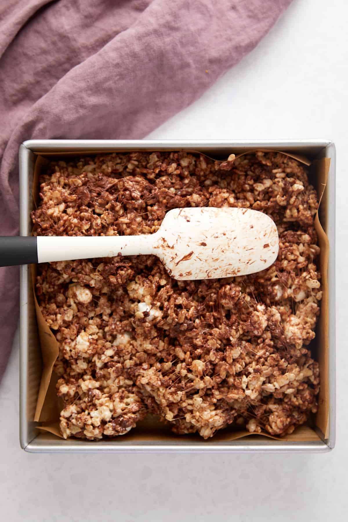 Overhead view of Chocolate chip Rice Krispie treats in pan being spread out with a spatula.
