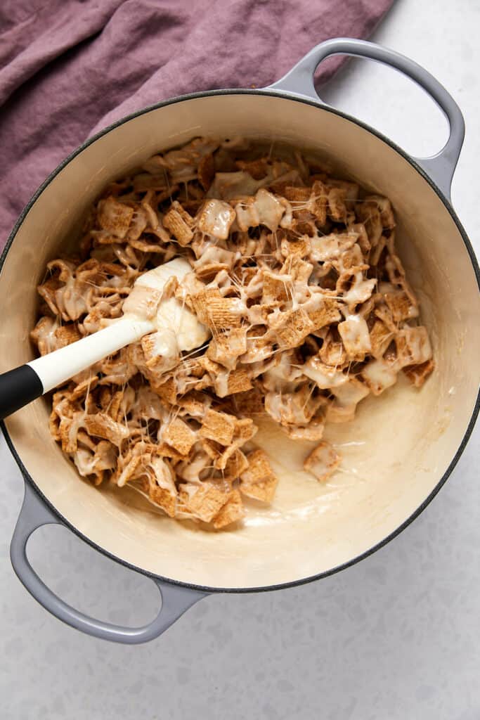 Overhead view of cinnamon toast crunch cereal being mixed with melted marshmallows with a spatula.