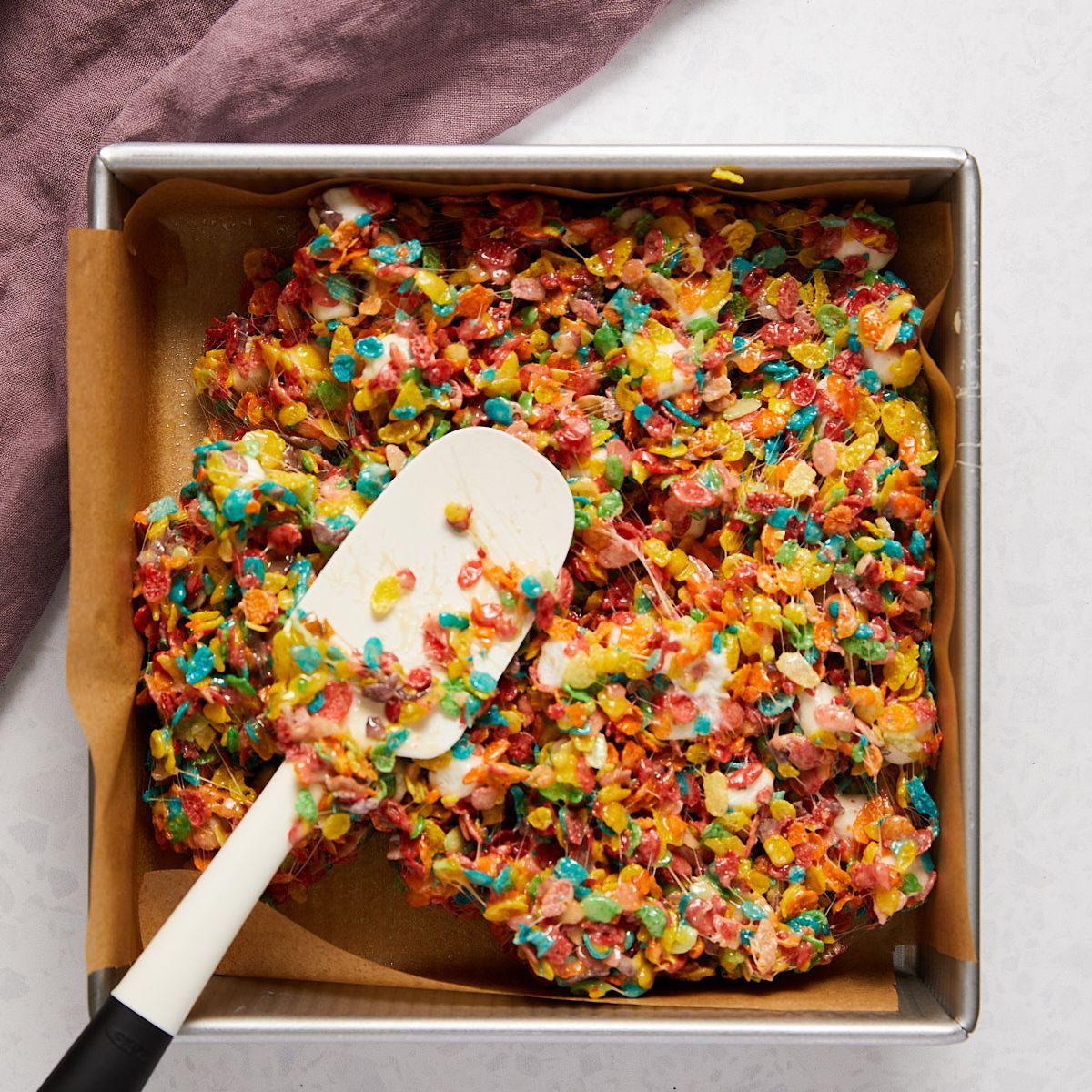 Fruity pebbles treats mixture pressed into a parchment-lined pan.