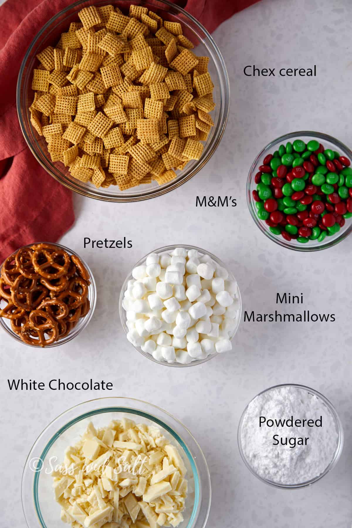 Overhead view of white chocolate Christmas Chex mix with M&M's ingredients in glass bowls.