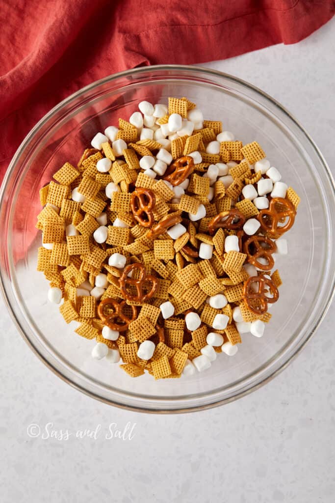 Overhead view of Chex mix, pretzels, and mini marshmallows mixed in a glass bowl.