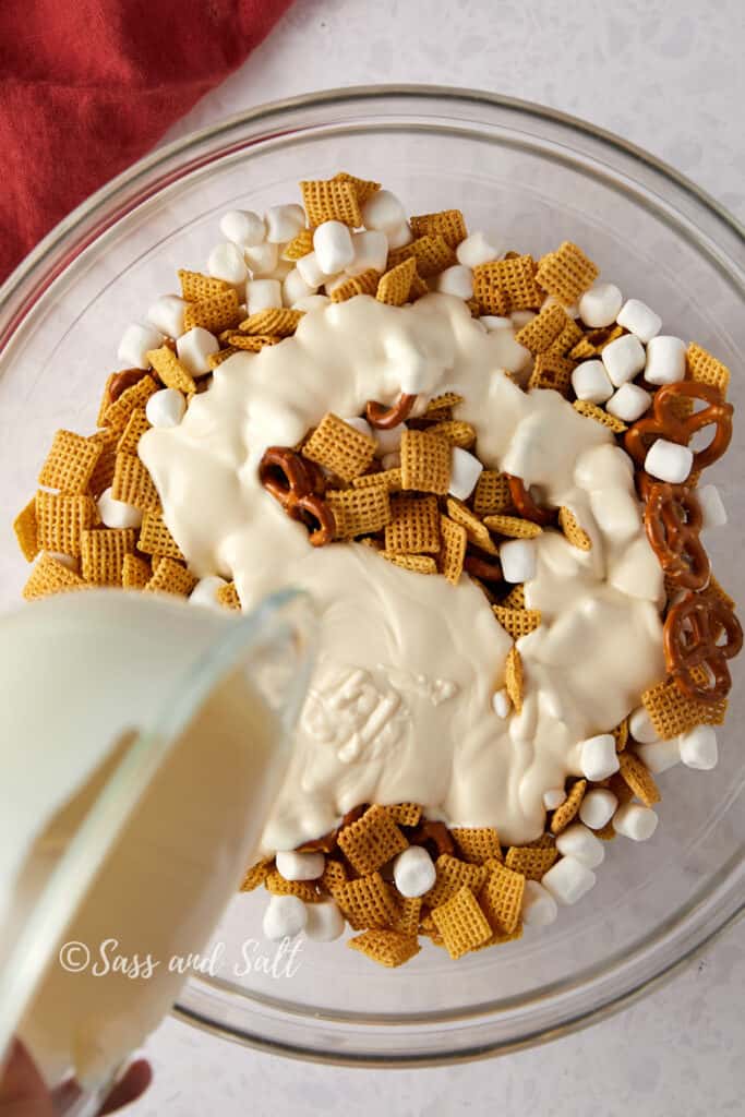 Overhead view of white chocolate being poured over Chex mix.