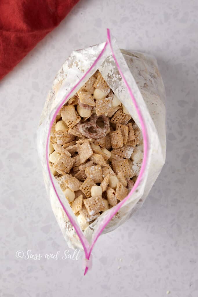 White chocolate Chex mix in a plastic bag with powdered sugar.