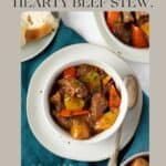 The image is a promotional graphic featuring a hearty beef stew recipe. The text at the top reads "WARM UP YOUR SOUL WITH THIS HEARTY BEEF STEW." Below the text is a photograph of a white bowl filled with beef stew, with visible chunks of beef, carrots, and potatoes, garnished with chopped parsley. A spoon rests beside the bowl, and another bowl of stew and a piece of bread are in the background, all atop a teal cloth. The watermark "Sass and Salt" and the website "www.thesassandsalt.com" are displayed, directing viewers to the source of the recipe.