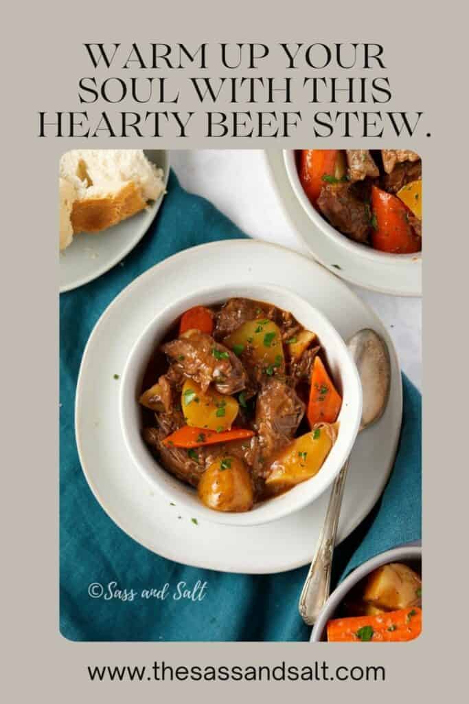 The image is a promotional graphic featuring a hearty beef stew recipe. The text at the top reads "WARM UP YOUR SOUL WITH THIS HEARTY BEEF STEW." Below the text is a photograph of a white bowl filled with beef stew, with visible chunks of beef, carrots, and potatoes, garnished with chopped parsley. A spoon rests beside the bowl, and another bowl of stew and a piece of bread are in the background, all atop a teal cloth. The watermark "Sass and Salt" and the website "www.thesassandsalt.com" are displayed, directing viewers to the source of the recipe.