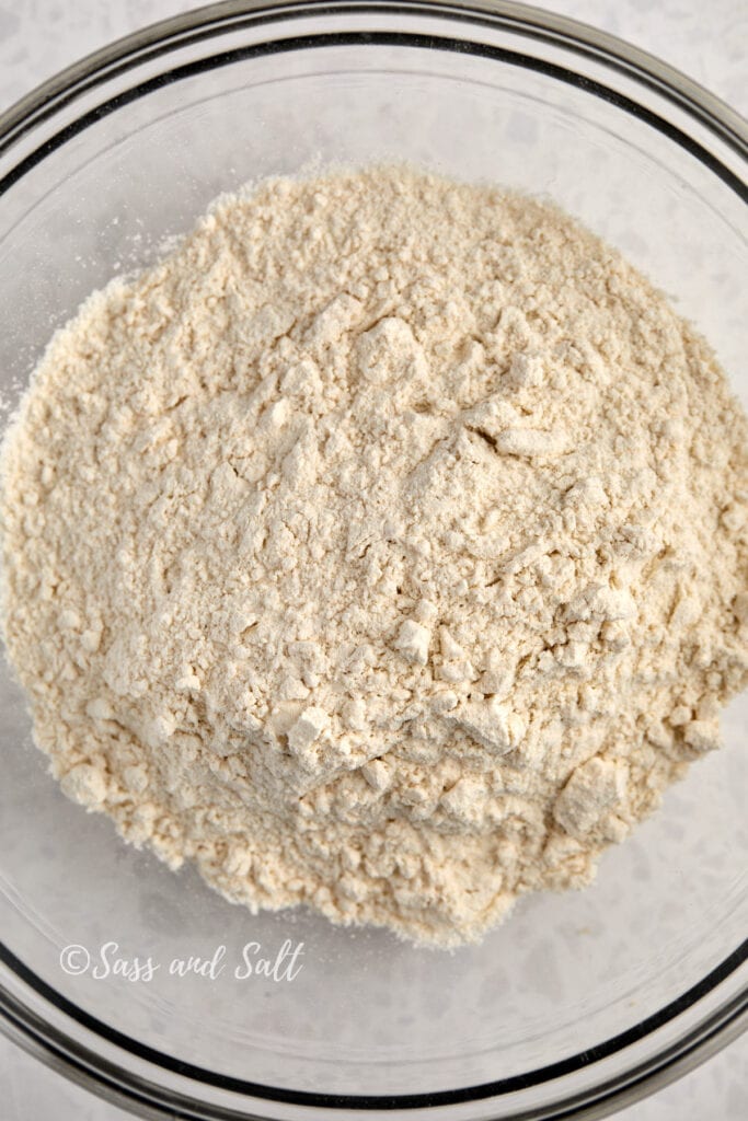 The image shows a clear glass bowl containing all-purpose flour. 