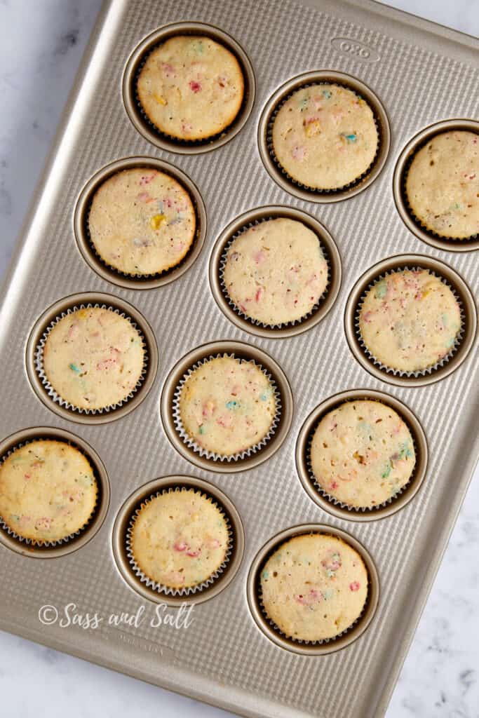 Baked Fruity Pebbles cupcakes with colorful speckles, in a gold cupcake tray, showcasing the baked treats' rise and texture.
