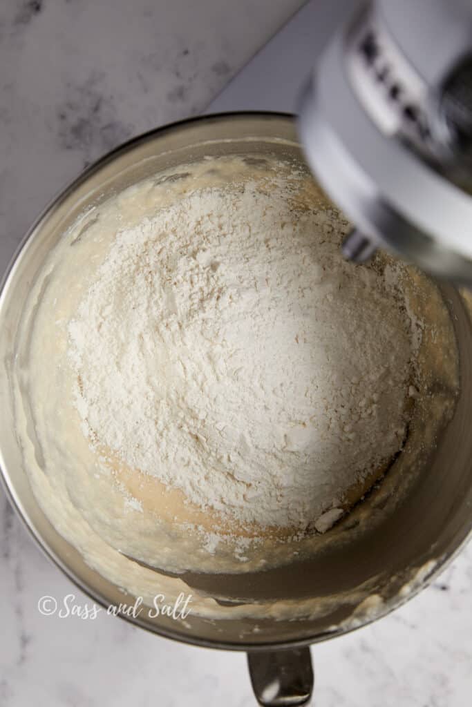 A mixer bowl containing flour added to wet ingredients in a mixer bowl.