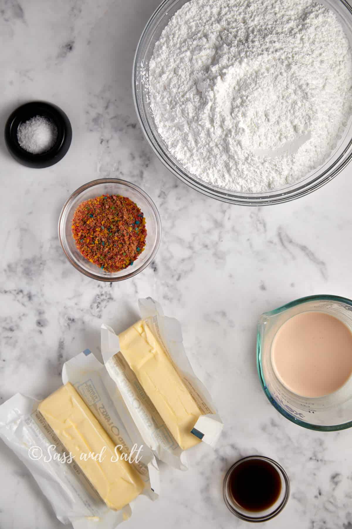 Ingredients for baking arranged on a marble countertop, including flour, seasoning, butter, milk, and vanilla extract, ready for a cooking recipe.