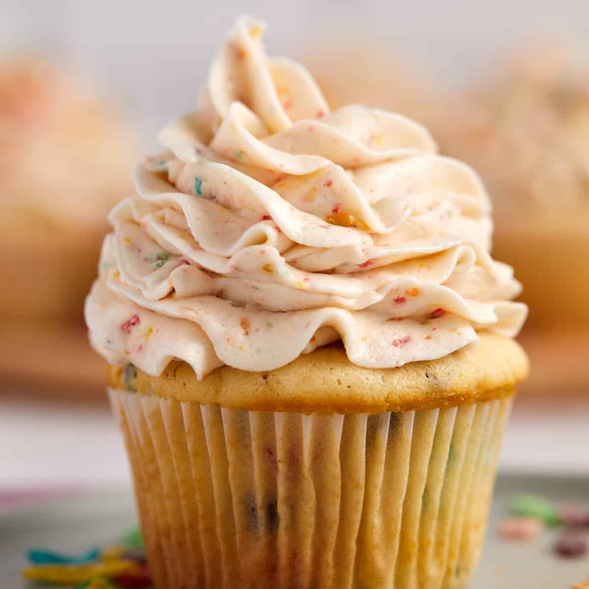 A close-up of a vanilla cupcake topped with a swirl of creamy, fruity pebbles-infused frosting, hinting at a delightful, sweet treat.
