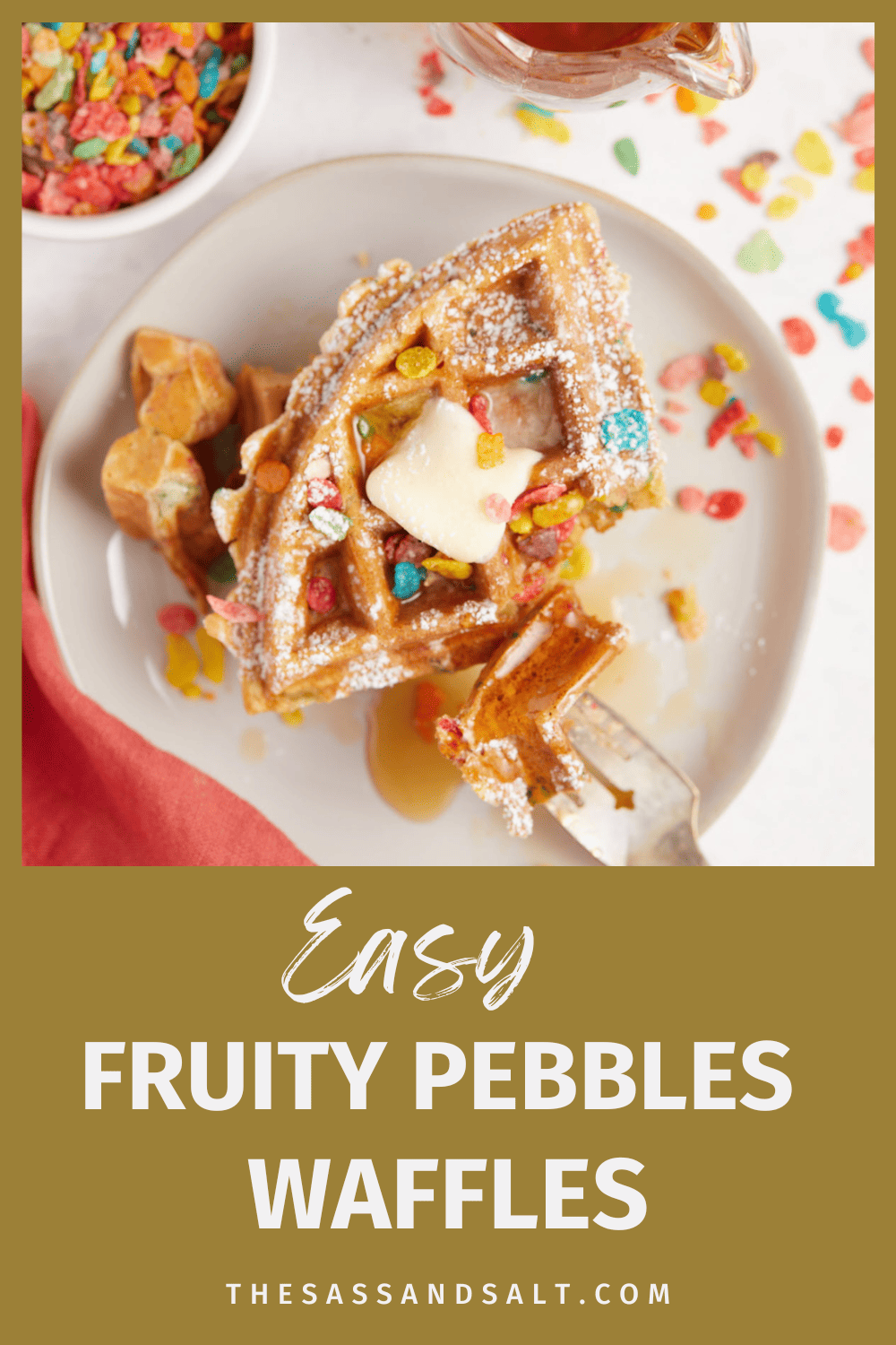 A plate of Fruity Pebbles waffles topped with colorful fruity pebbles cereal, a sprinkle of powdered sugar, and a drizzle of maple syrup.