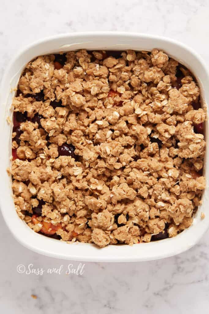 A rectangular dish of freshly baked fruit crisp with a golden-brown oat topping, displayed on a white marble surface.