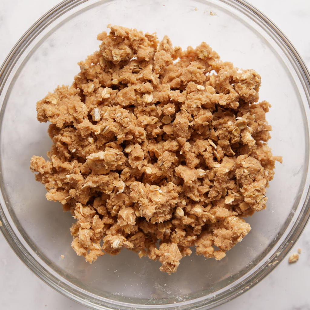 A glass bowl of buttery oat crumble topping for cherry peach crisp.
