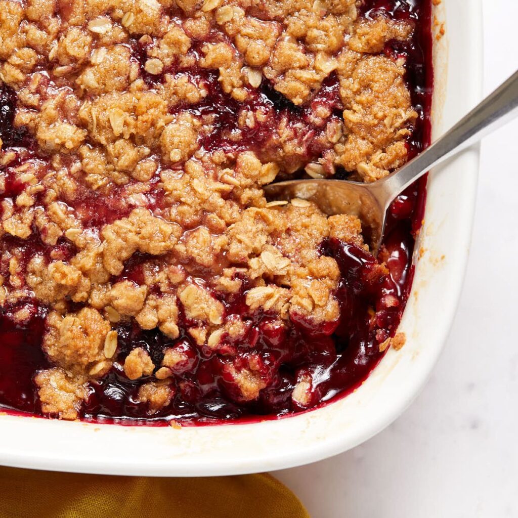 Baked peach cherry crisp with a golden oat topping, scooped to show the juicy peach and cherry filling underneath.