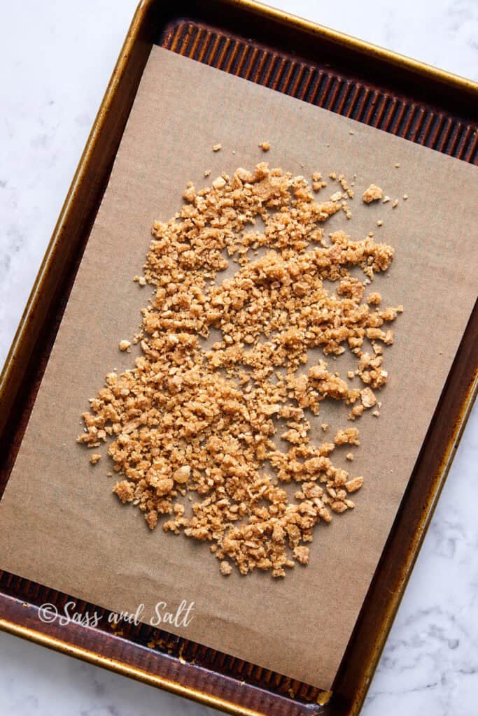 A baking sheet lined with parchment paper cinnamon toast crunch mix. The surface beneath the baking sheet is a white, marble-textured countertop. 